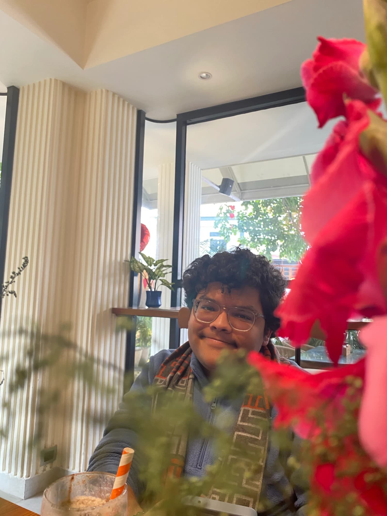 Parv Marwaha smiling at the camera from behind red flowers in a café